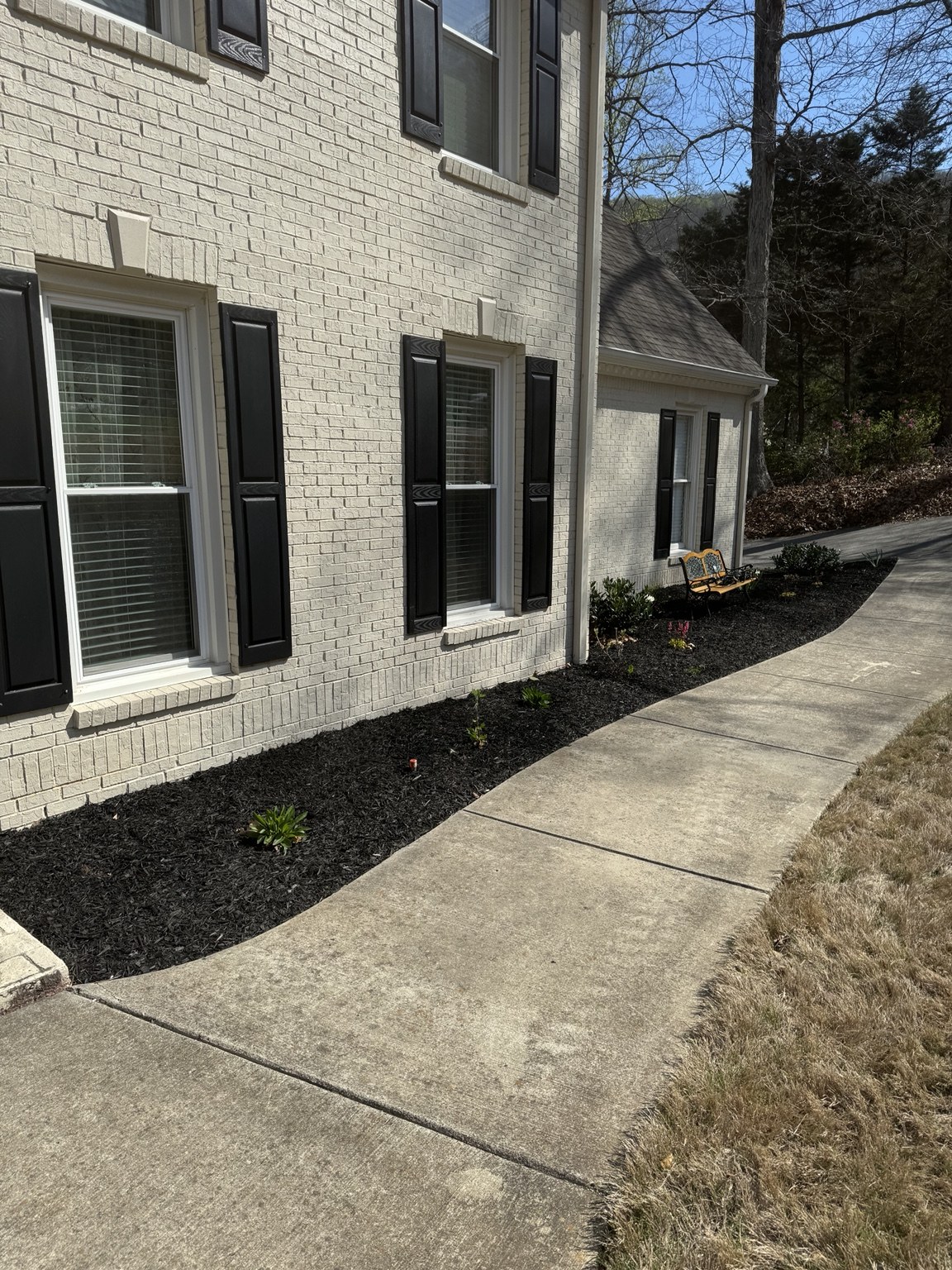 Freshly renewed foundation planting with a clean dark mulch finish beside a white brick residence